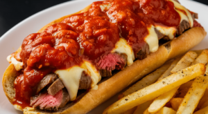 Traditional Philly cheesesteak sandwich topped with marinara sauce on a hoagie roll.