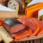 A gourmet platter featuring smoked-salmon ,paired with a variety of cheeses including Brie.