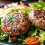 A grilled beef patty served on a plate with healthy sides like vegetables and a whole-grain bun.