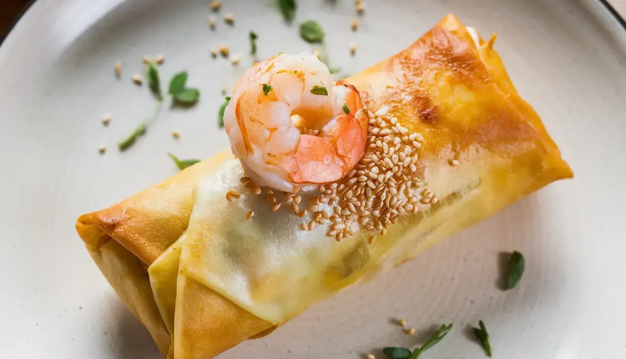 A plate with crispy shrimp egg rolls served with a dipping sauce.