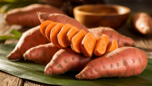 Sweet potatoes displayed next to regular potatoes on a wooden table