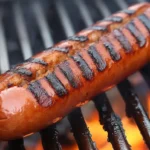 Grilled beef and pork hotdogs on a plate with condiments