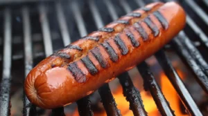 Grilled beef and pork hotdogs on a plate with condiments