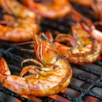 Shrimp cooking on a grill with shells on, showing char marks.